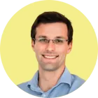 Homme avec des lunettes souriant, vêtu d'une chemise bleu clair, sur fond de cercle jaune.