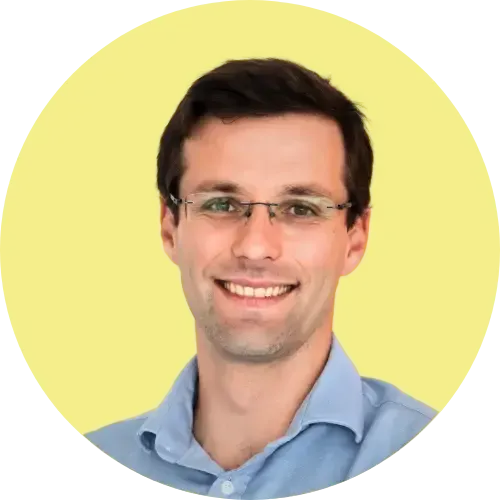 Homme avec des lunettes souriant, vêtu d'une chemise bleu clair, sur fond de cercle jaune.