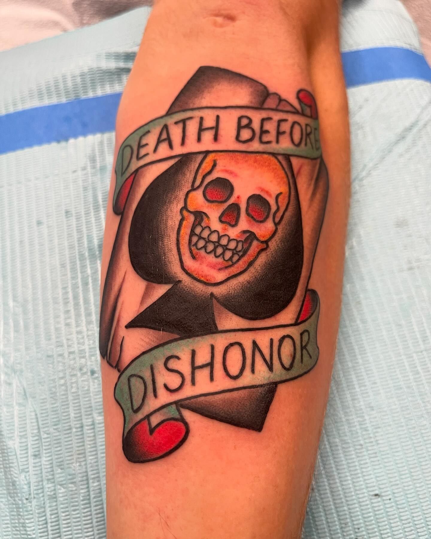 A person has a tattoo of a spade shape with a skull on their arm