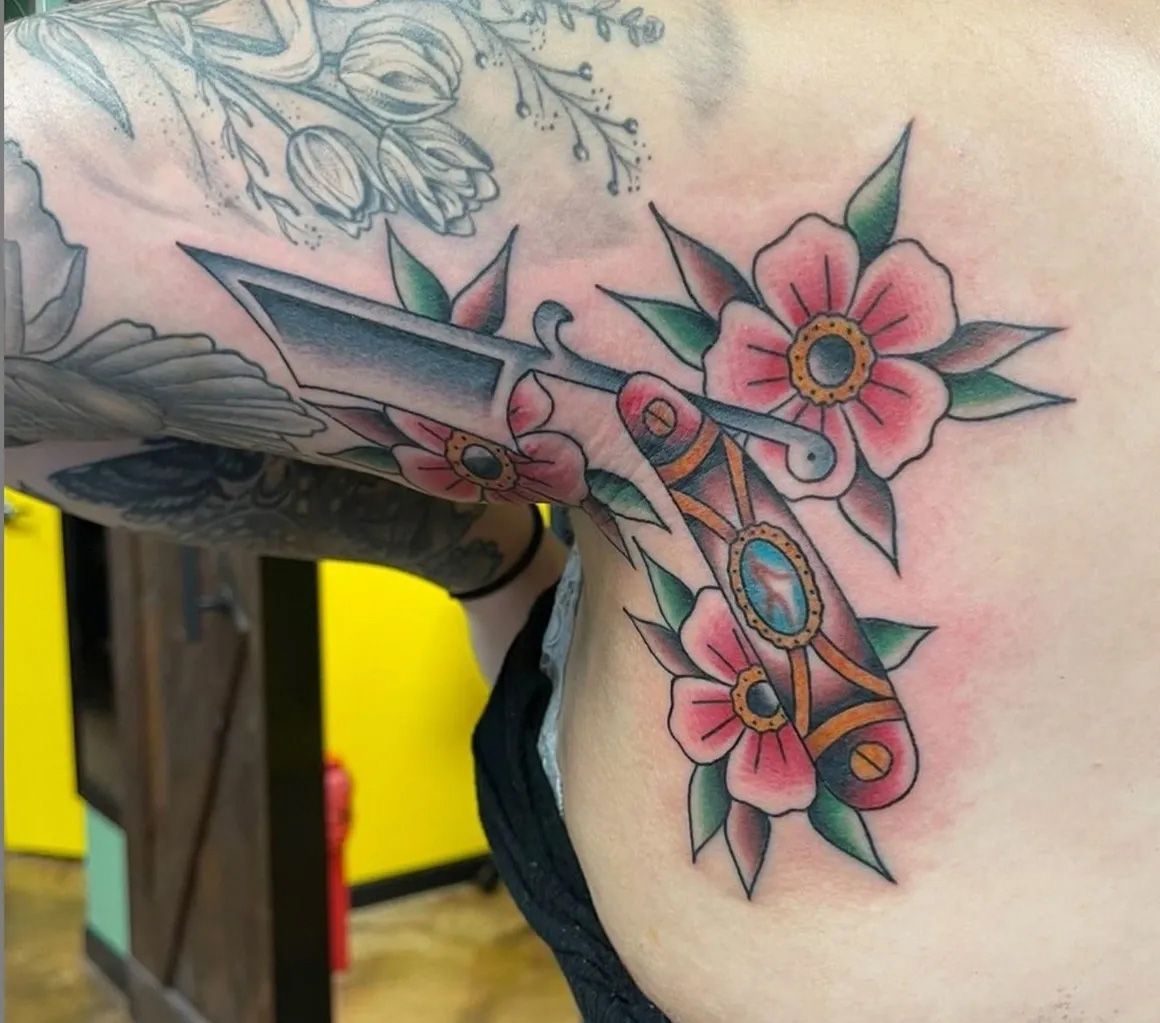 A woman has a tattoo of flowers and a razor on her underarm