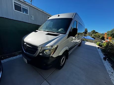 Silver cargo van parked on a concrete driveway in front of a house on a sunny day.