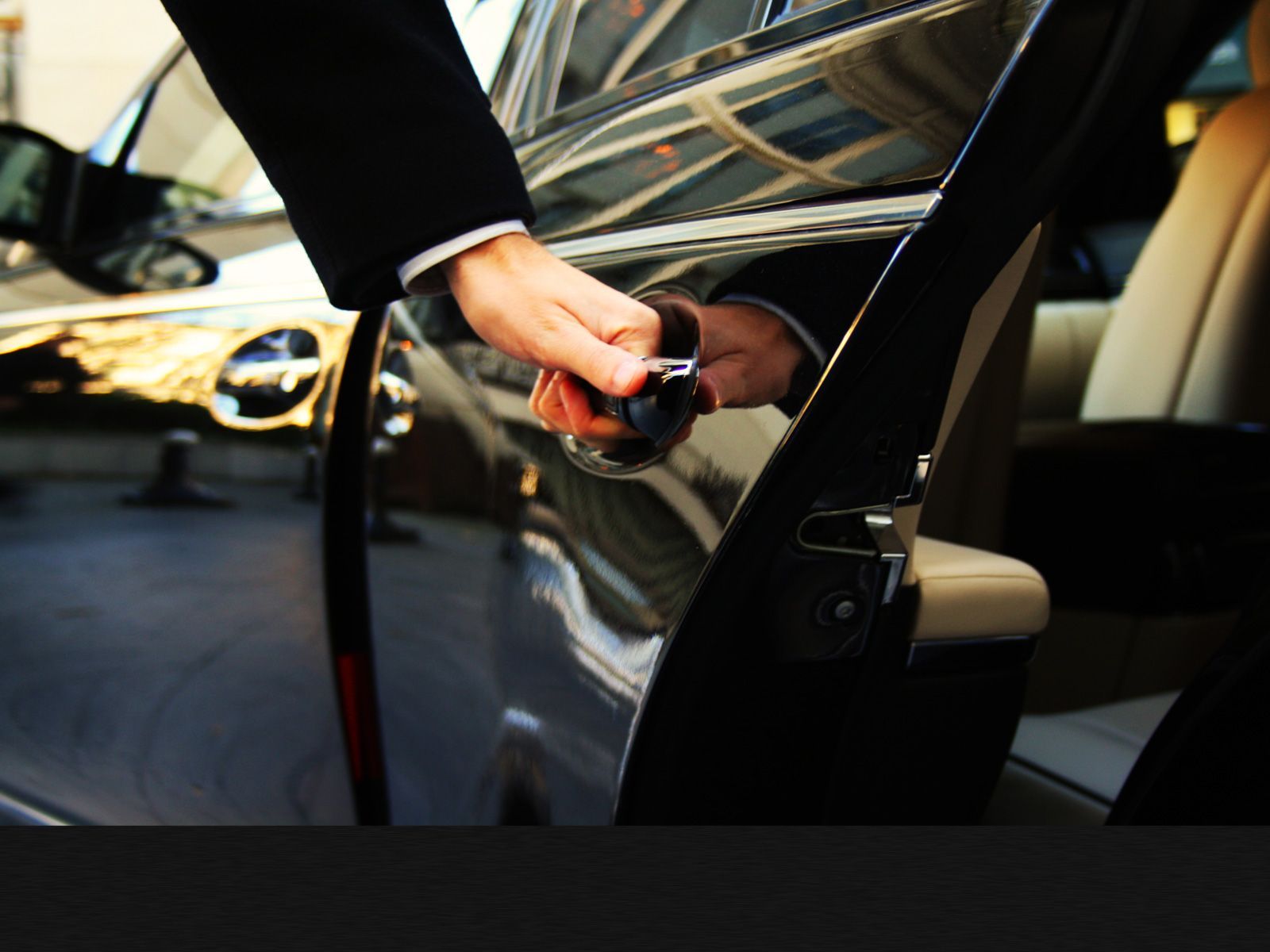 Person in a suit opening a black car door, possibly for a passenger.