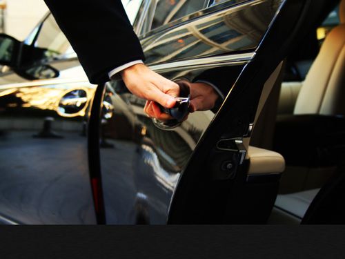 Person in a suit opening a black car door, possibly for a passenger.