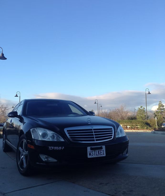 Black Mercedes-Benz sedan parked on a sidewalk under a blue sky, with streetlights in the background.