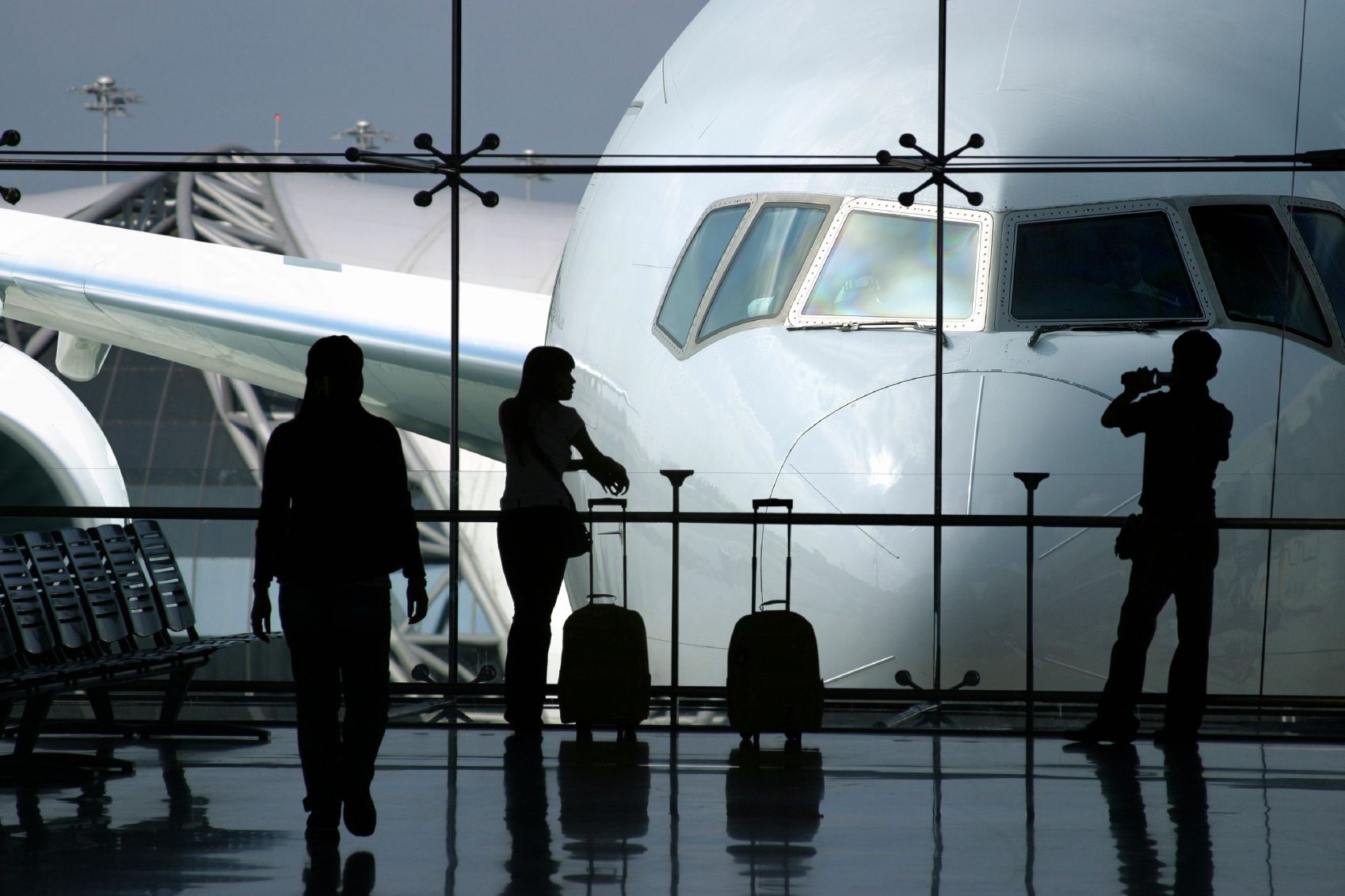 People in a terminal near an airplane, silhouetted. Passengers with luggage.