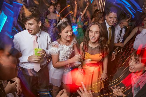 People dancing at a party with flashing lights. One girl in a white dress, another in orange, are smiling.