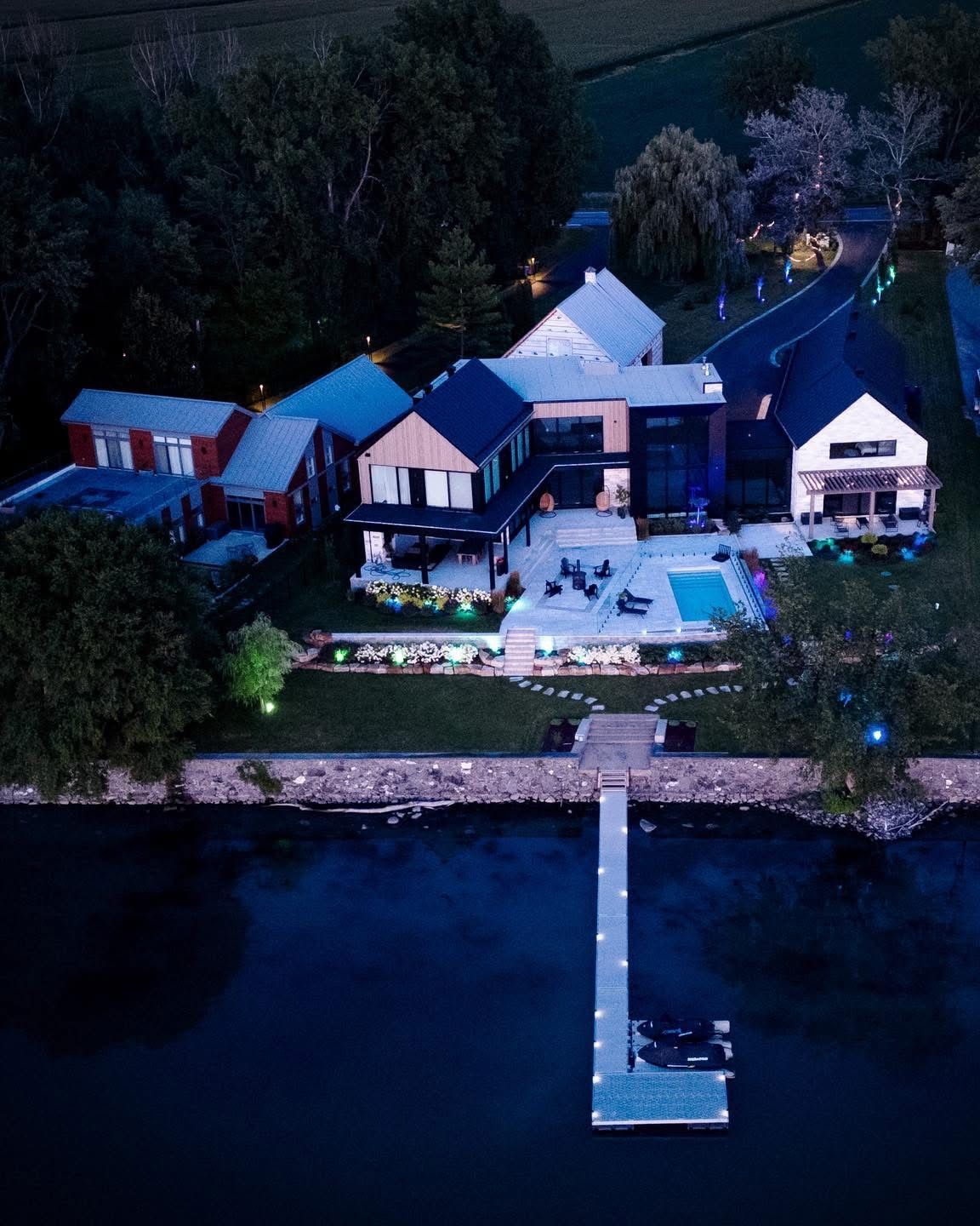 Modern waterfront home at dusk with dock and pool.