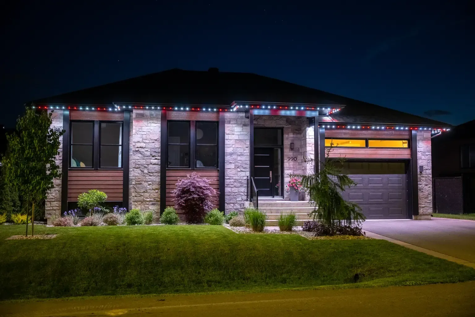 House exterior at night, lit with red, white, and blue lights above windows and garage door.