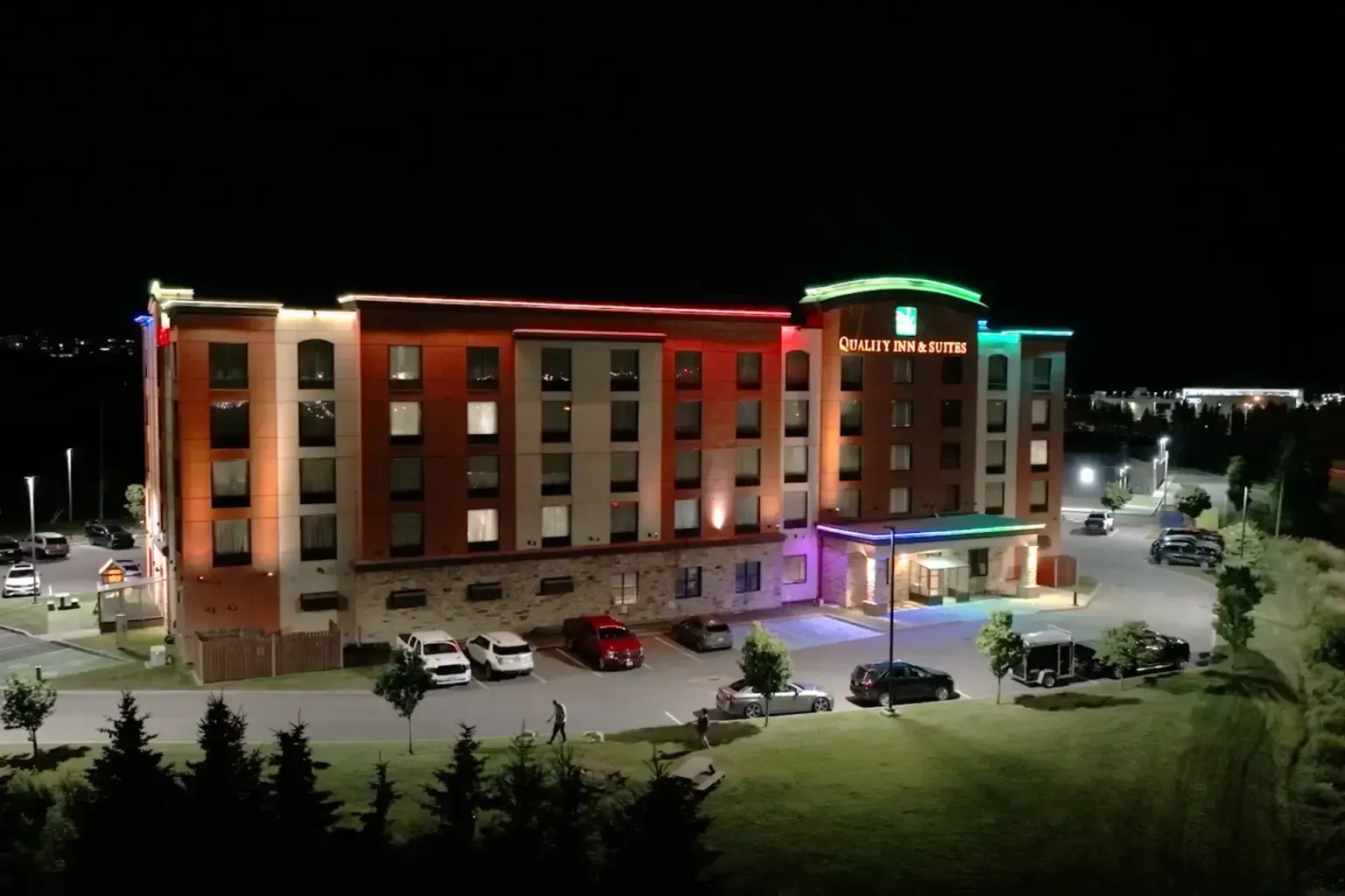 A brightly lit hotel at night with colorful lights and cars parked in front.