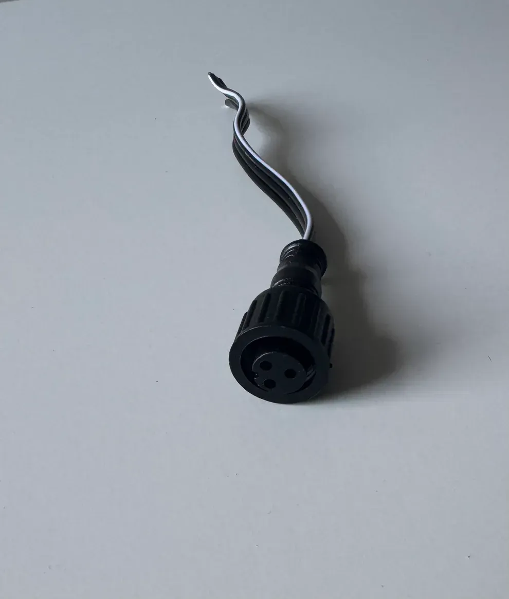 Black 3-pin electrical connector with two wires extending from the top, set against a white surface.