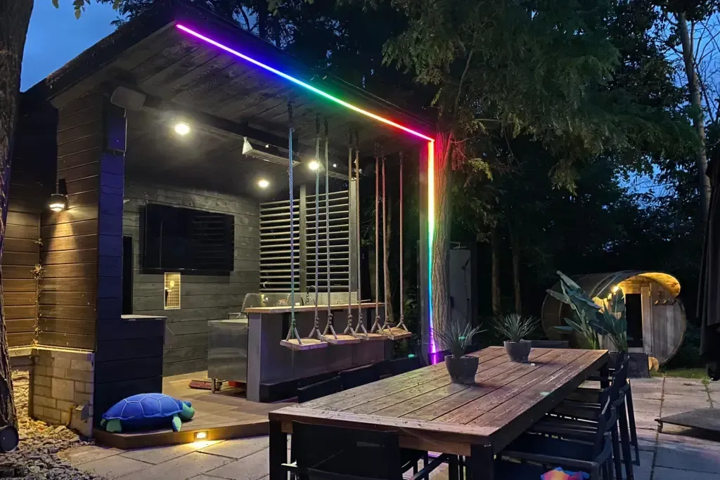 Outdoor entertainment area with rainbow LED lights around a structure. Table and swings visible.