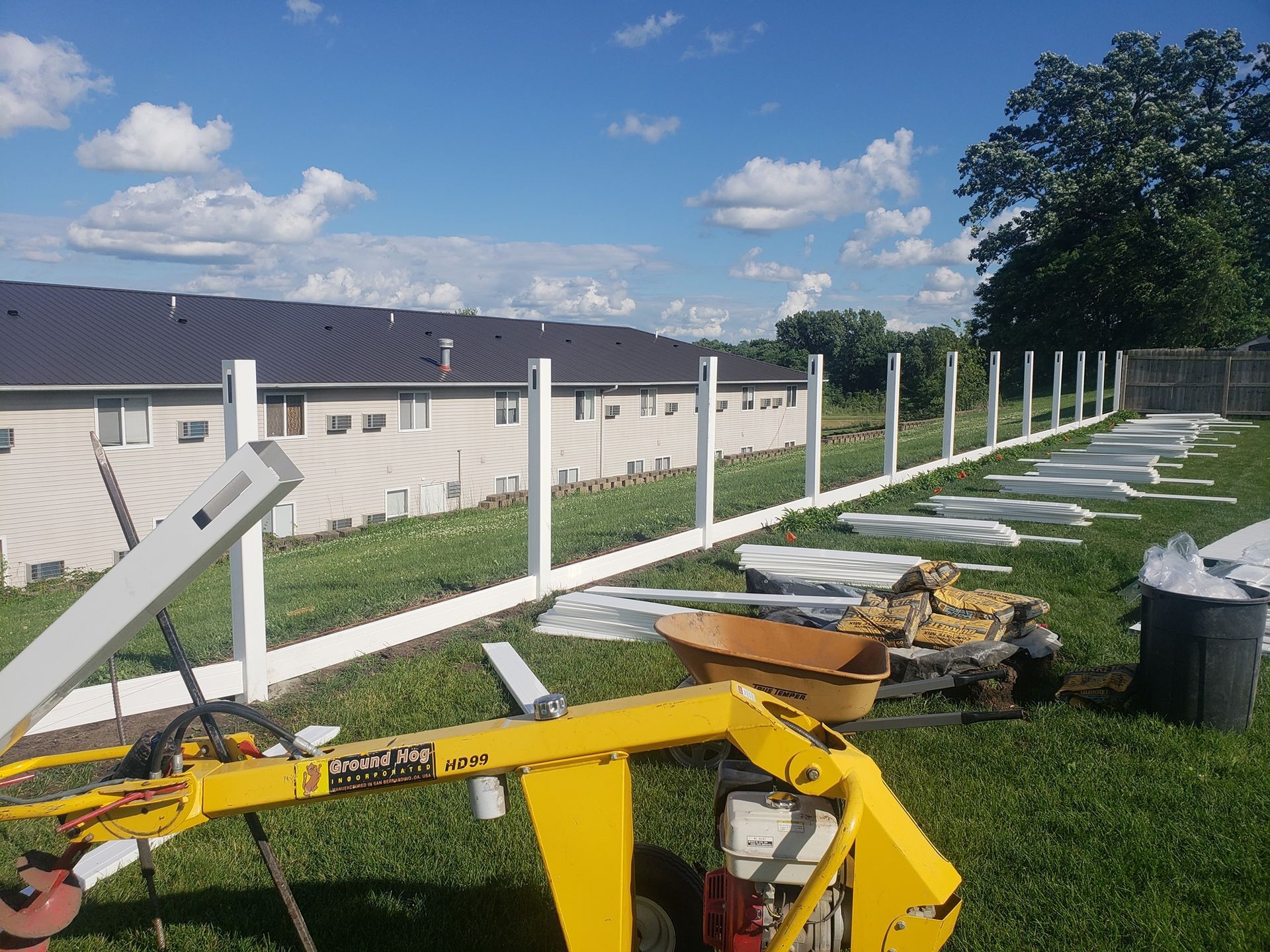 A yellow tractor is parked in front of a white fence being built.