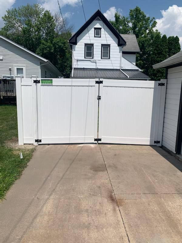 A white fence surrounds a driveway in front of a house.
