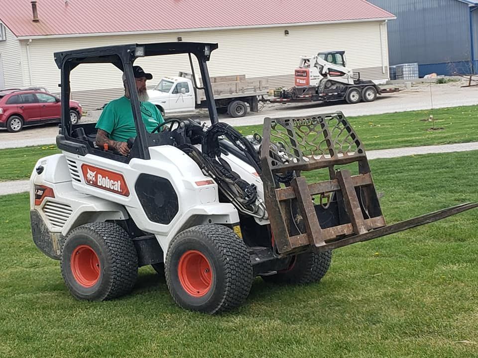 A man is driving a bobcat tractor on a lush green field.