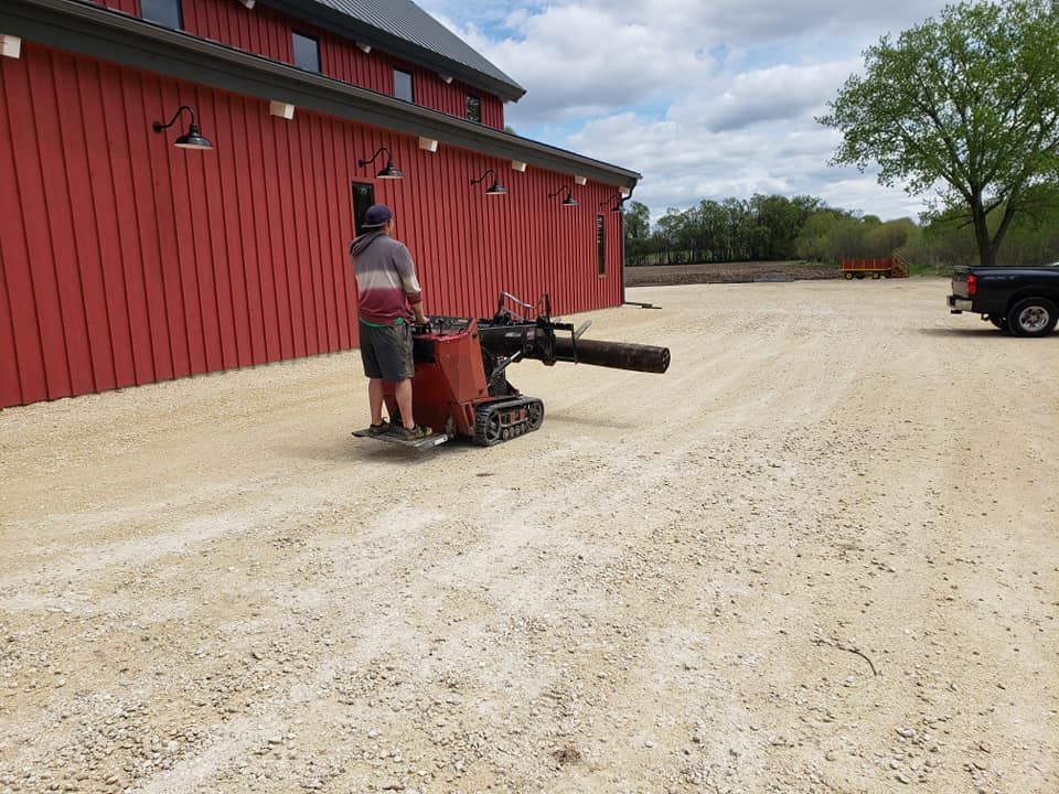 A man is standing next to a machine in front of a red barn.