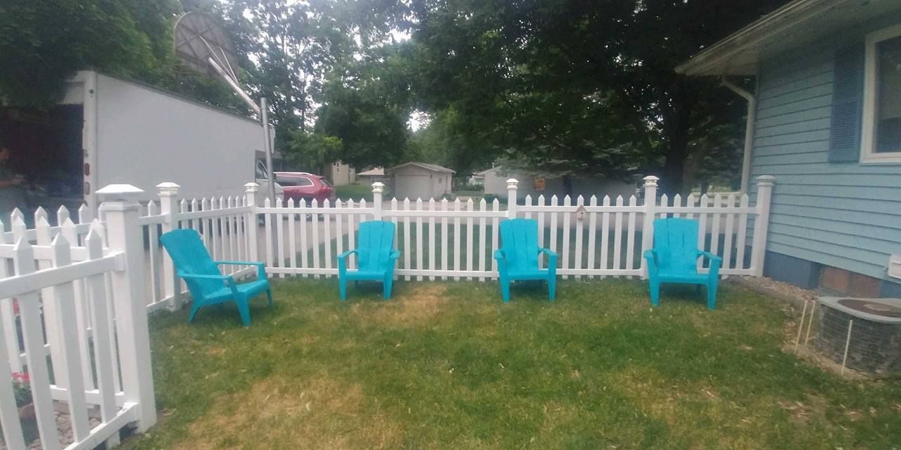 A white picket fence with blue chairs in front of it.