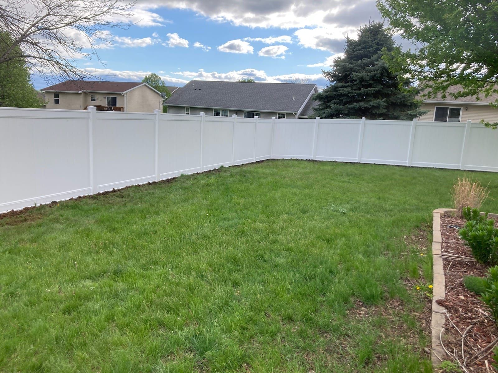 A white fence surrounds a lush green lawn in a backyard.