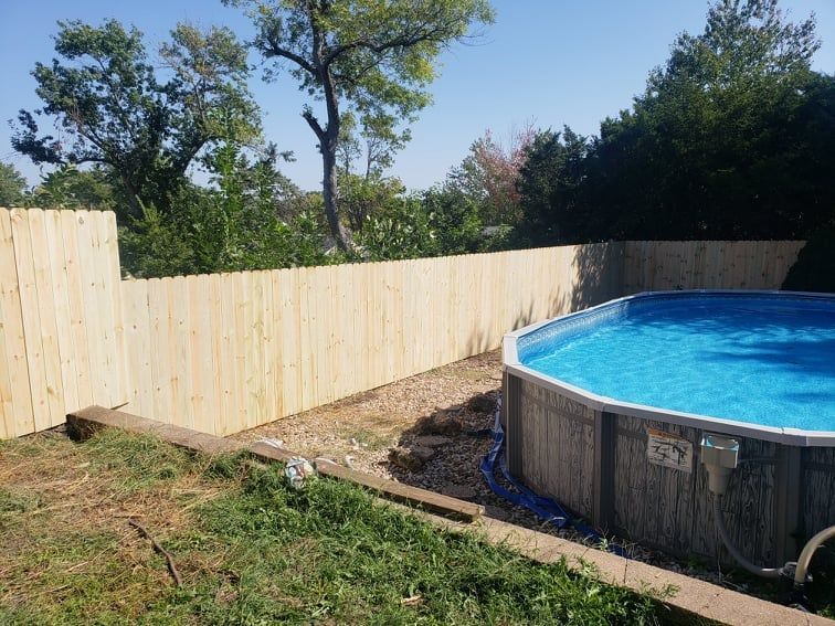A swimming pool is surrounded by a wooden fence in a backyard.