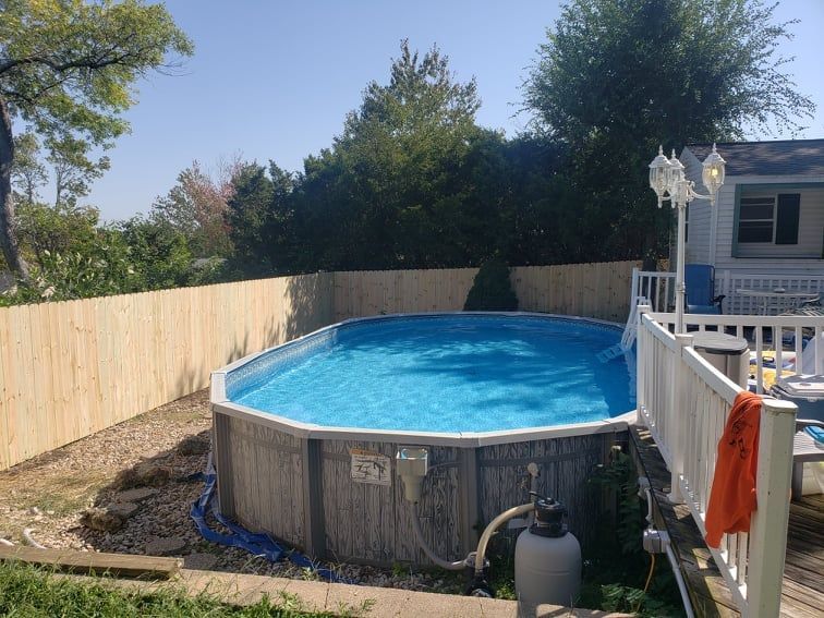 A large swimming pool is surrounded by a wooden fence in a backyard.