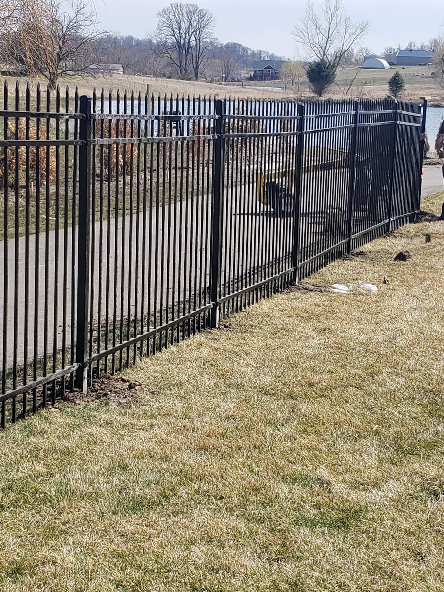 A black metal fence is sitting on top of a lush green field.