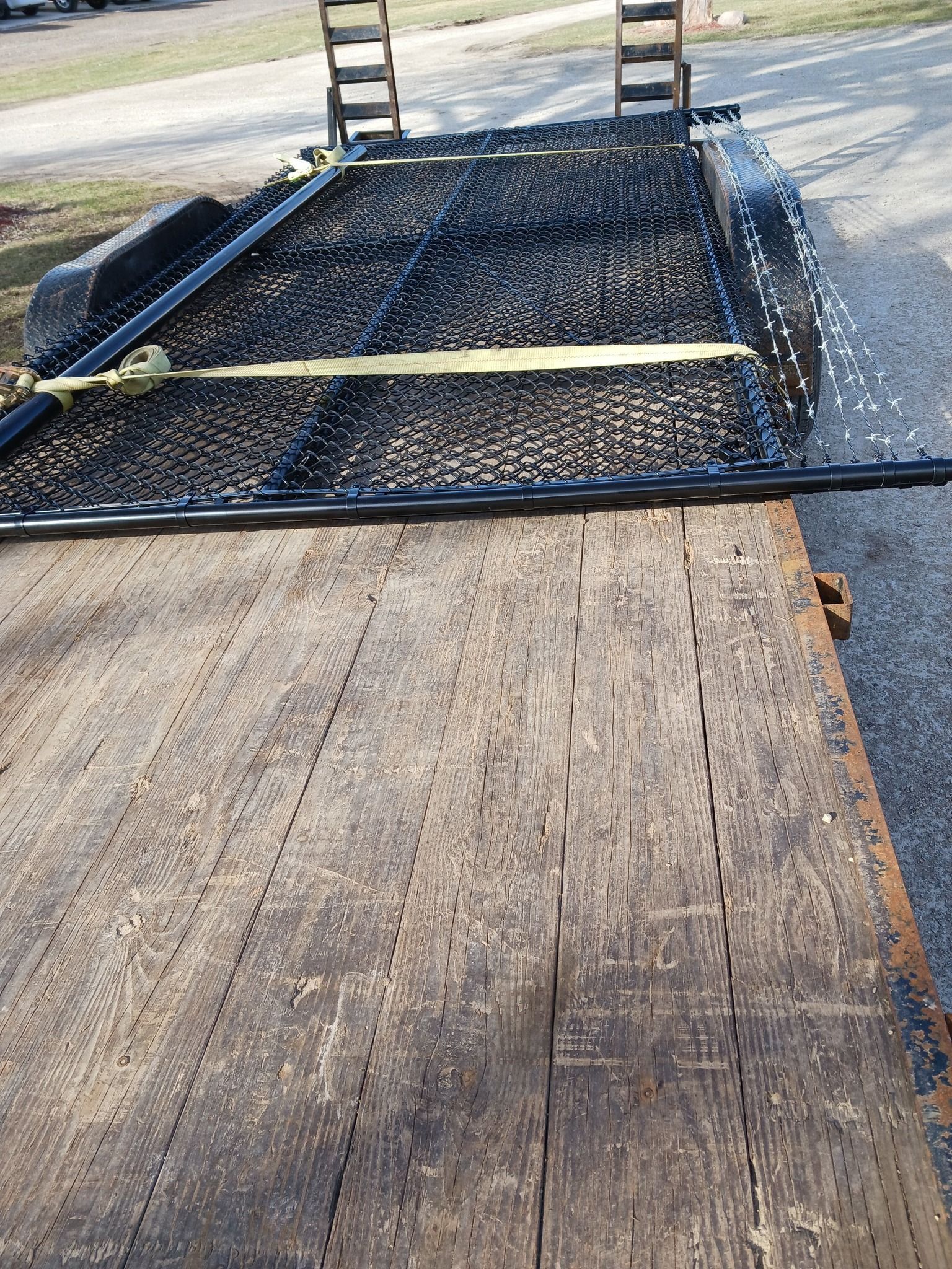 A wooden trailer with a chain link fence is parked on the side of the road.