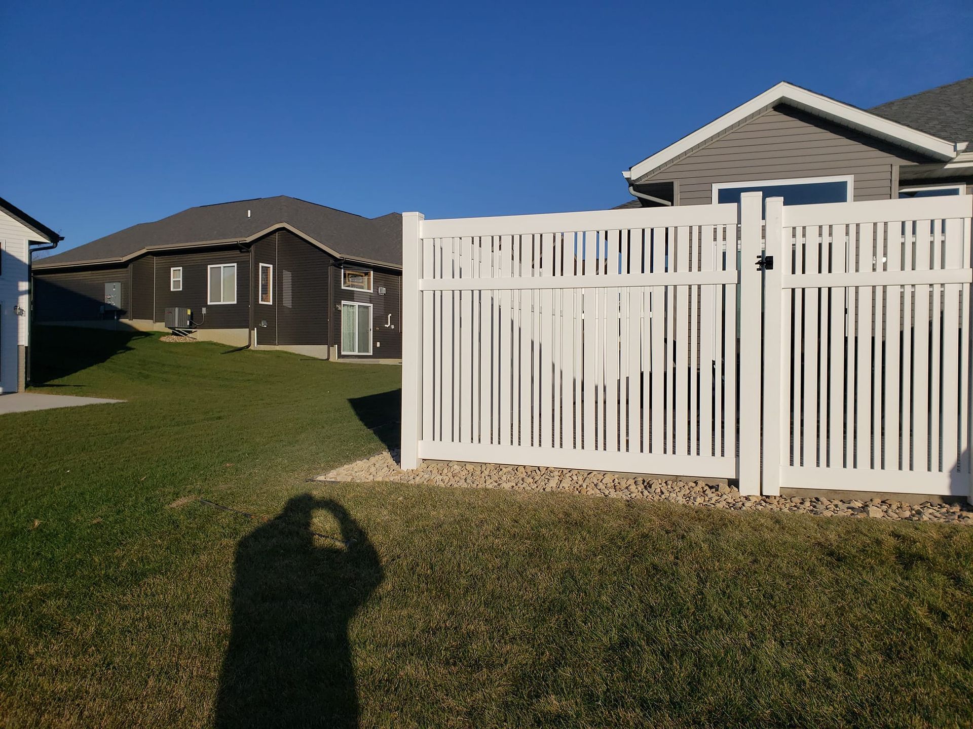 A shadow of a person is cast on a white fence in front of a house