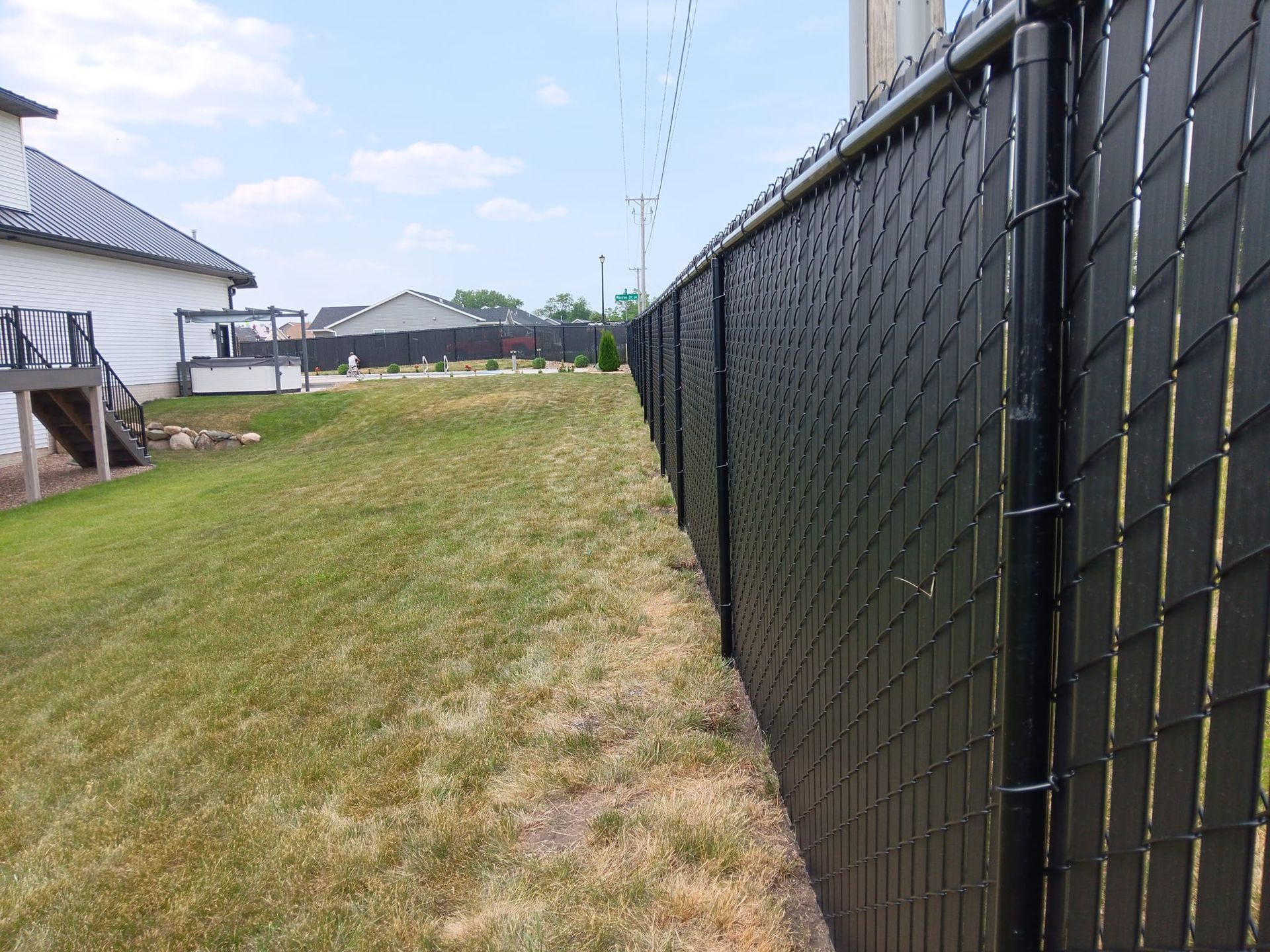 A black chain link fence surrounds a grassy yard in front of a house.