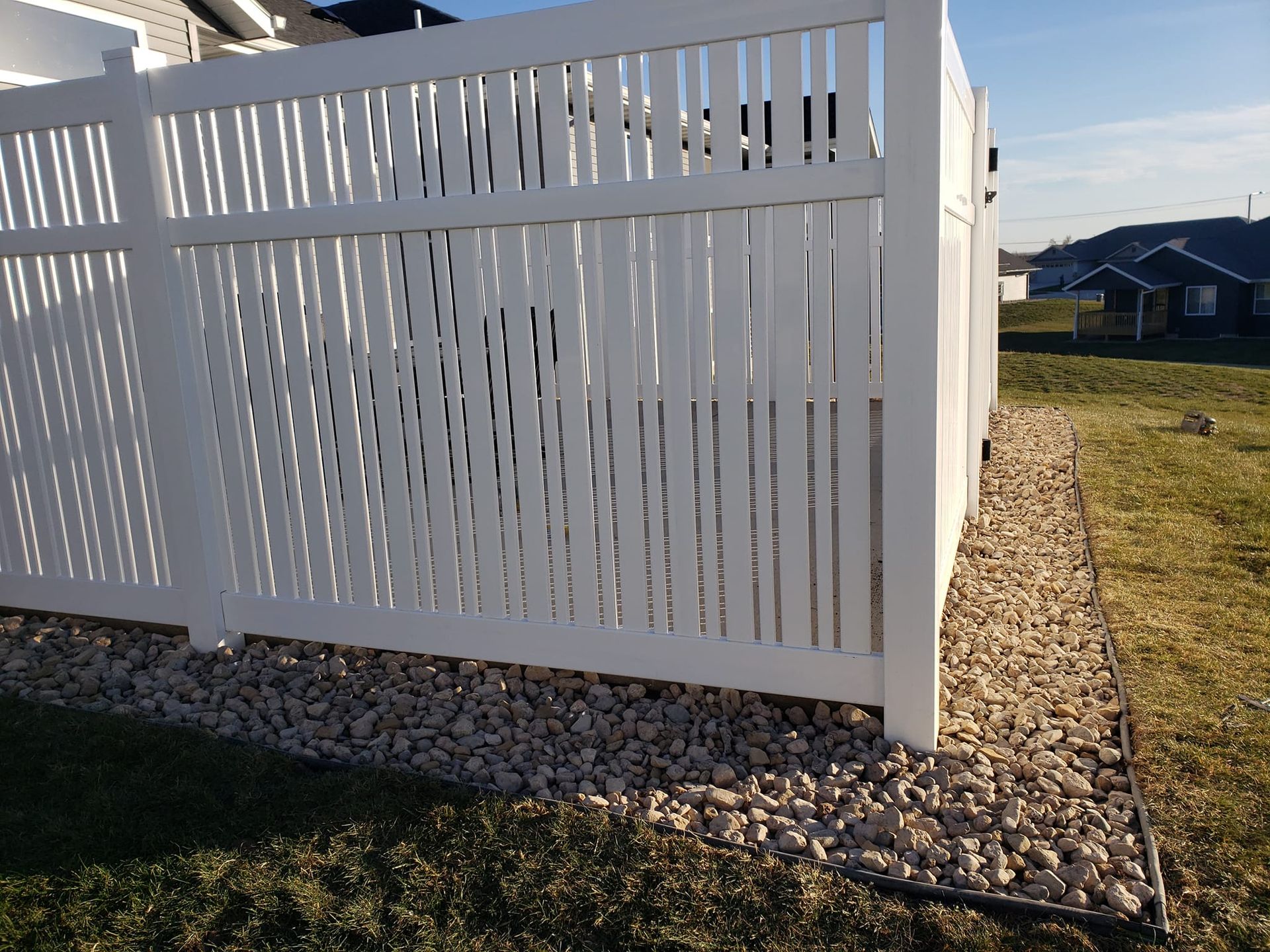 A white fence is surrounded by gravel and grass in a yard.