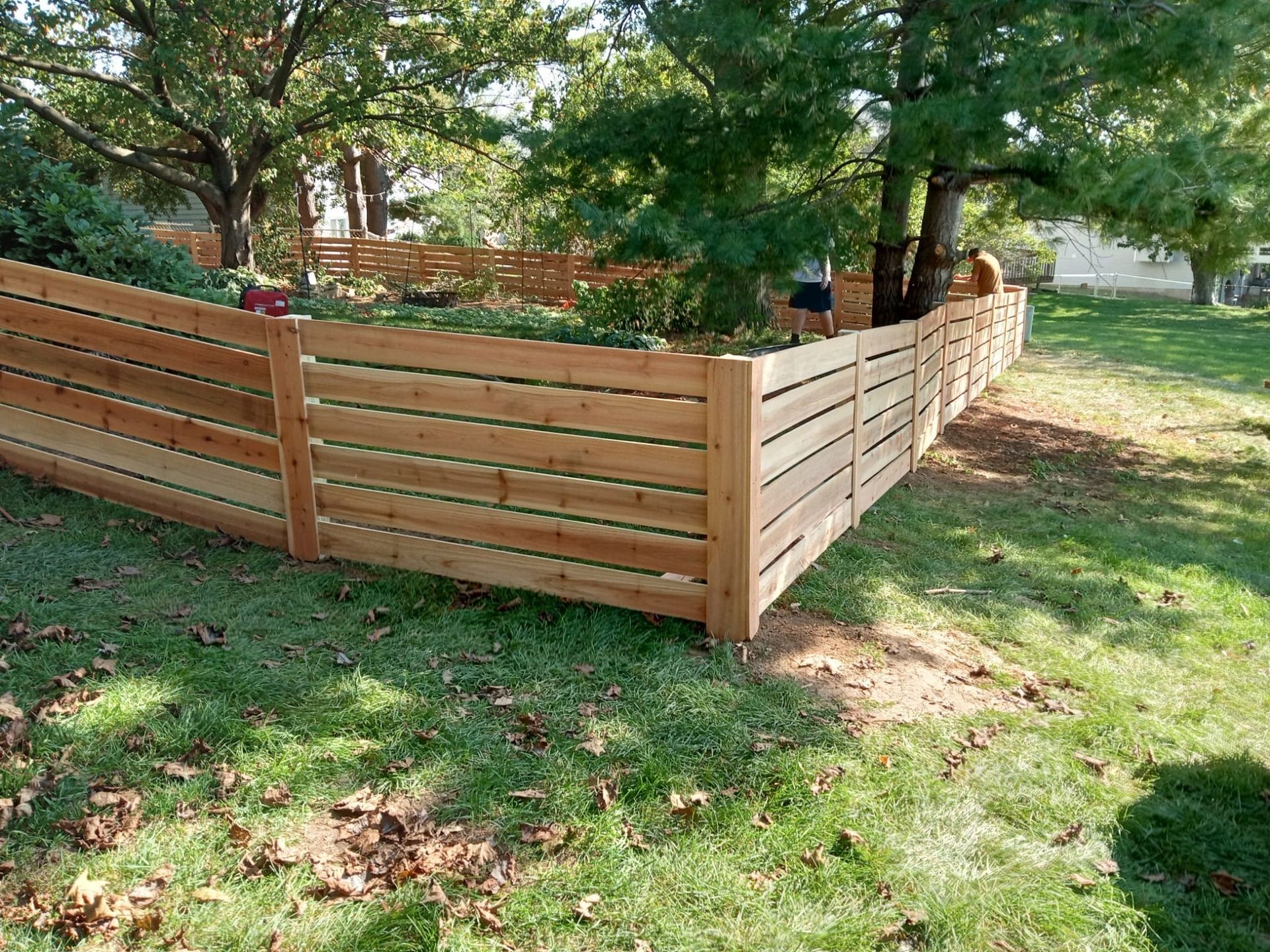 A wooden fence is in the middle of a lush green yard.