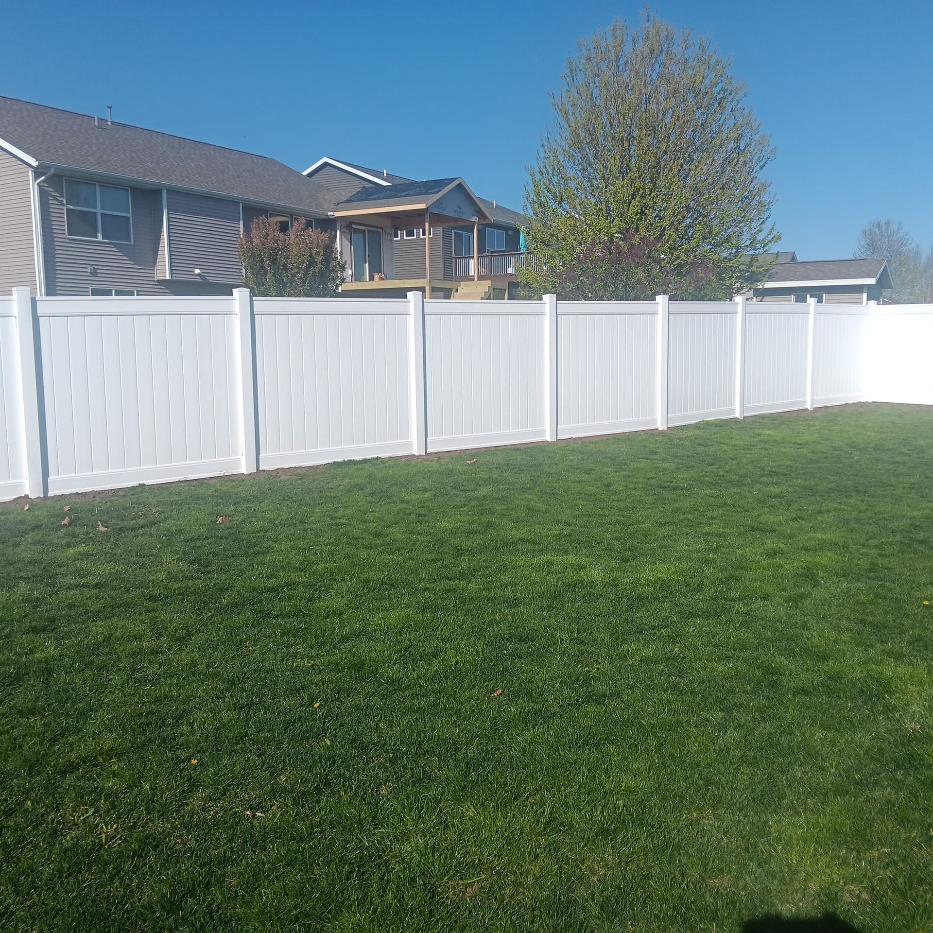 A white fence surrounds a lush green yard in front of a house.