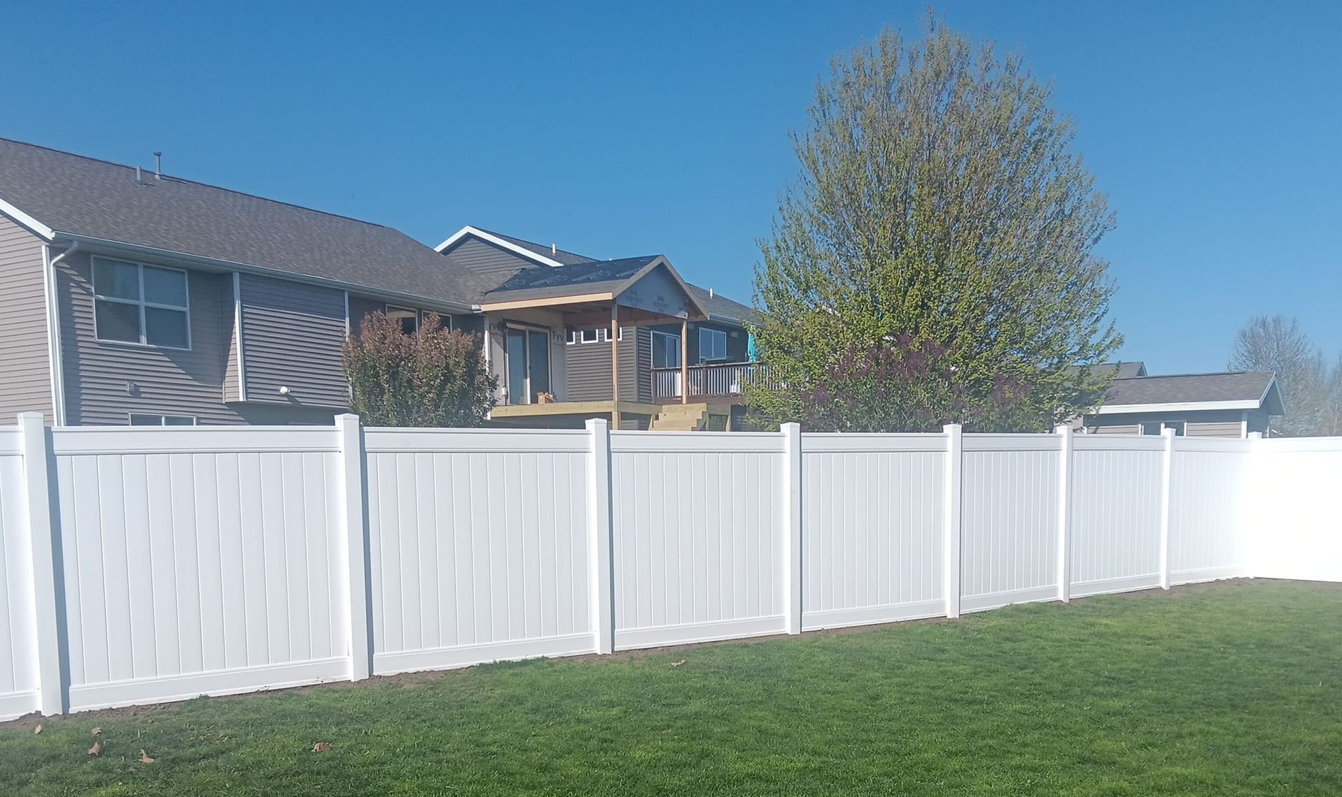 A white fence surrounds a lush green yard in front of a house.