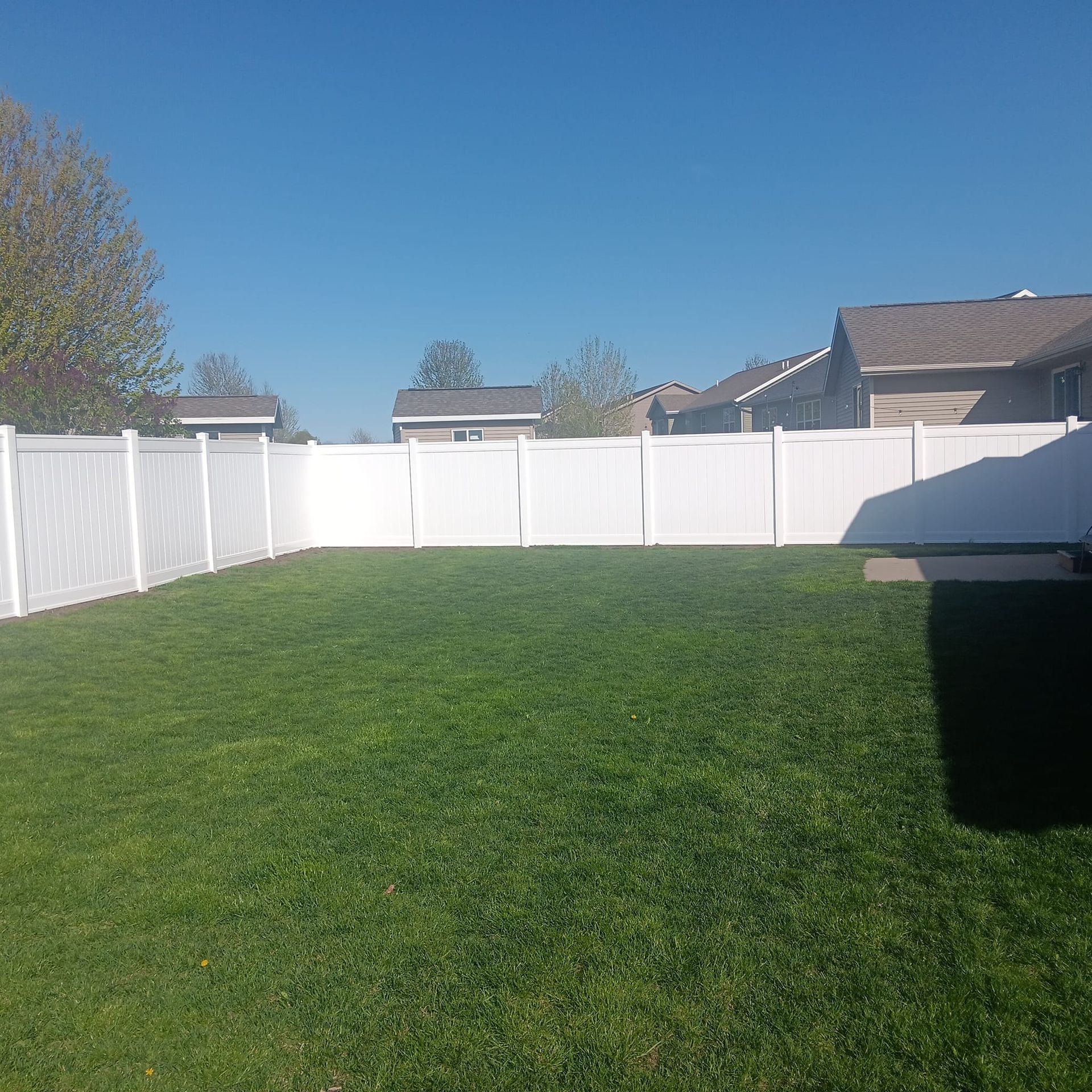A backyard with a white fence and a lush green lawn