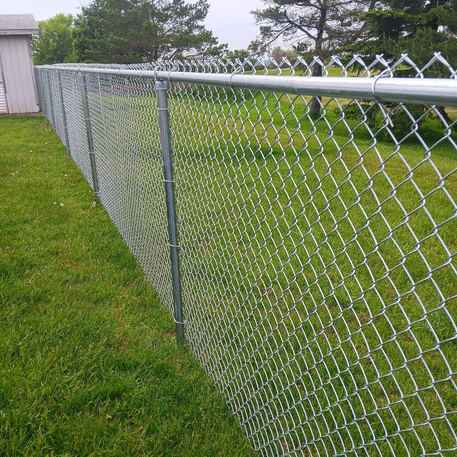 A chain link fence is sitting in the middle of a lush green field.