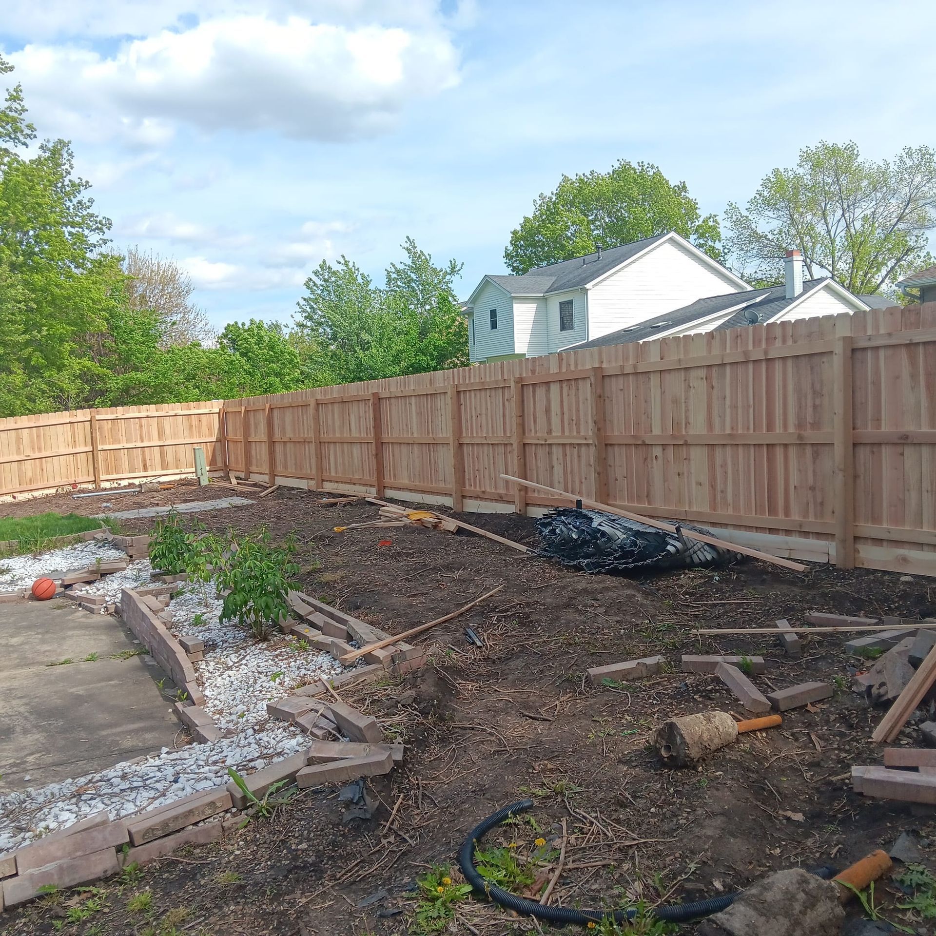 A wooden fence is surrounding a garden in a backyard.