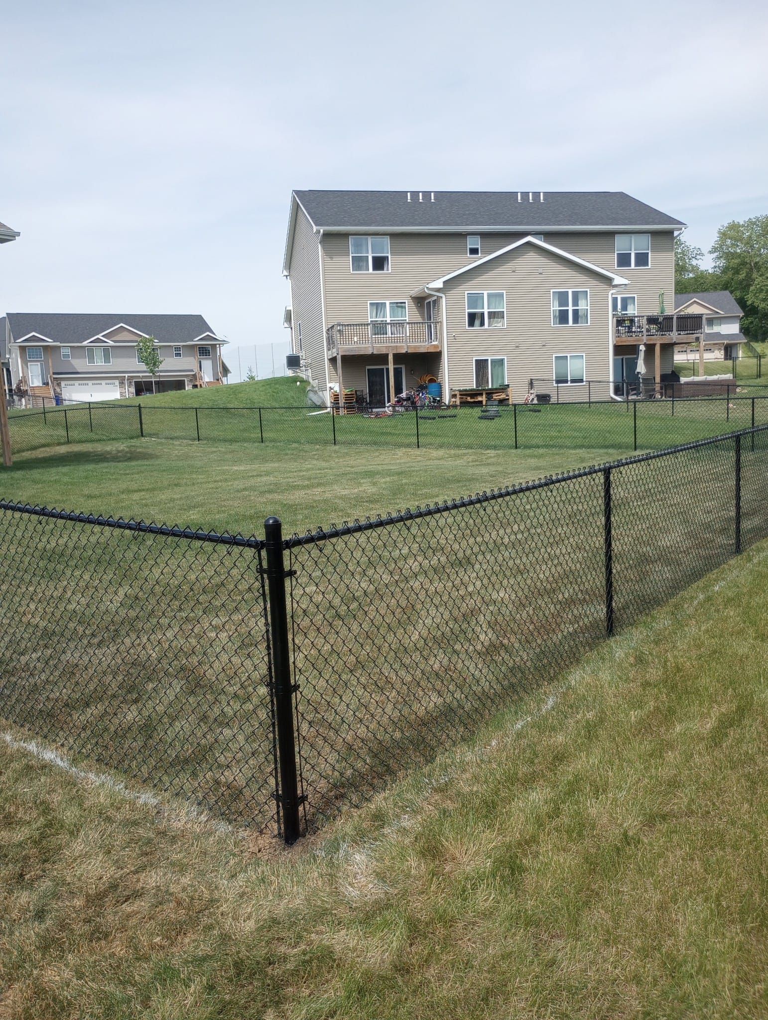 A chain link fence surrounds a lush green yard in front of a house.