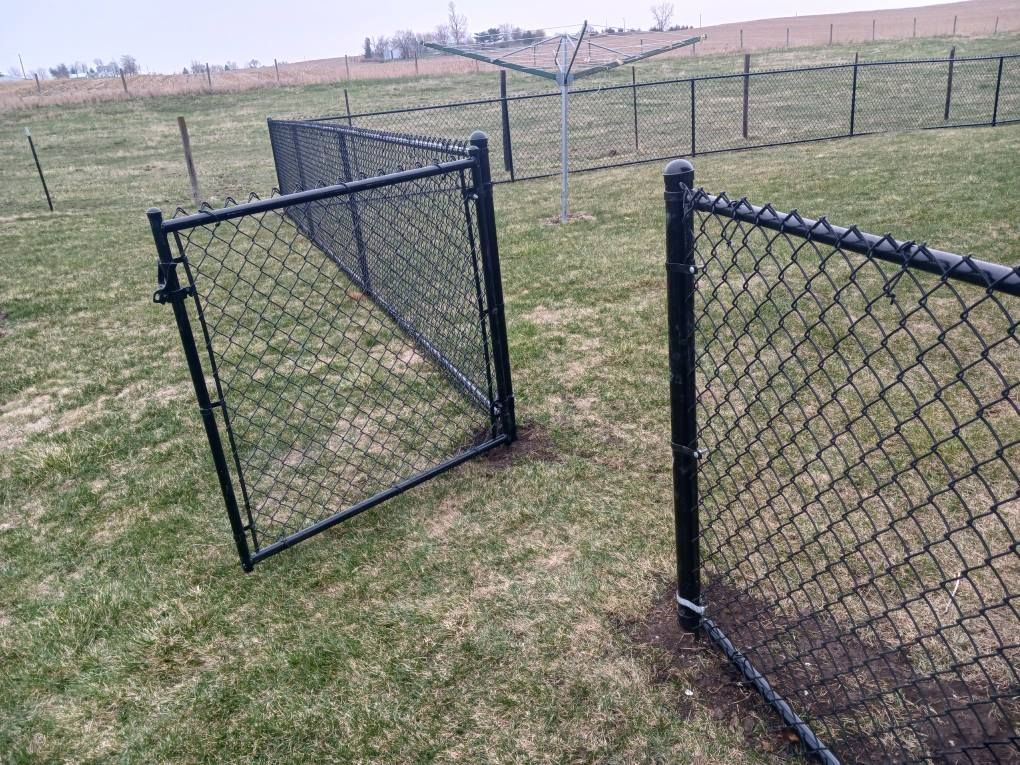 A chain link fence with a gate open in a grassy field.