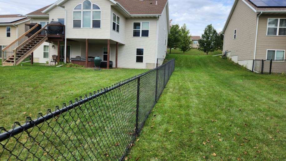 A chain link fence surrounds a lush green yard in front of a house.
