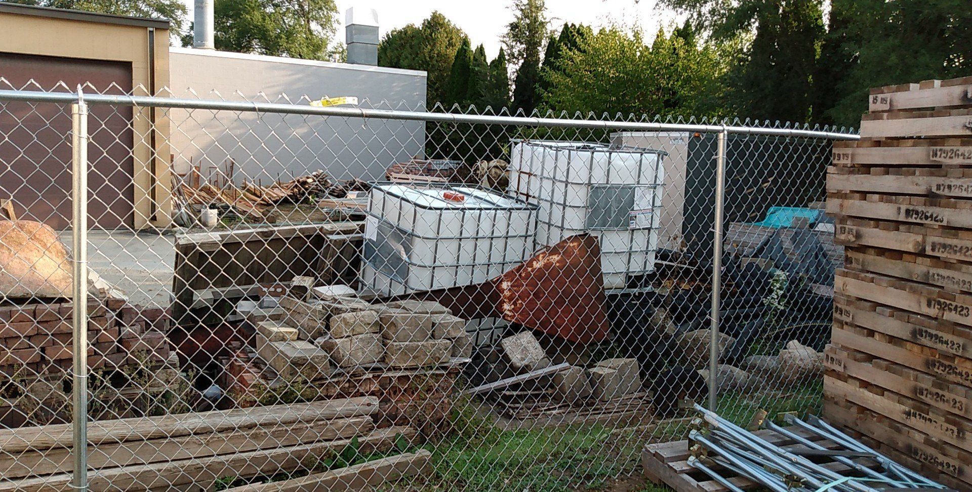 A chain link fence surrounds a pile of bricks and wooden pallets.