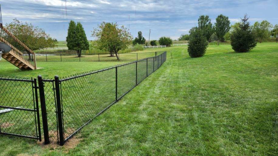 A chain link fence is in the middle of a lush green field.