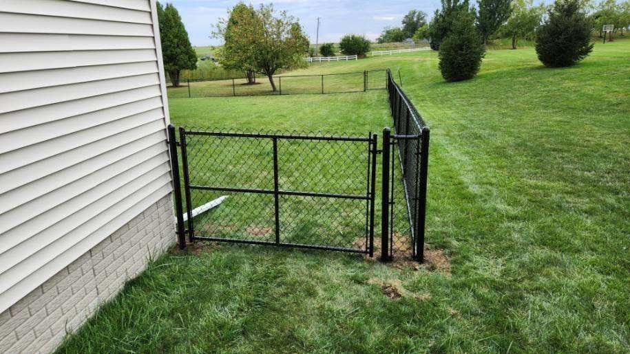 A chain link fence is surrounding a lush green yard next to a house.