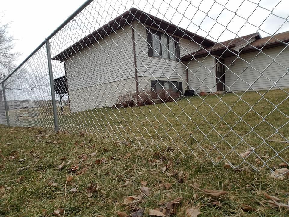 A chain link fence surrounds a house in a grassy yard.