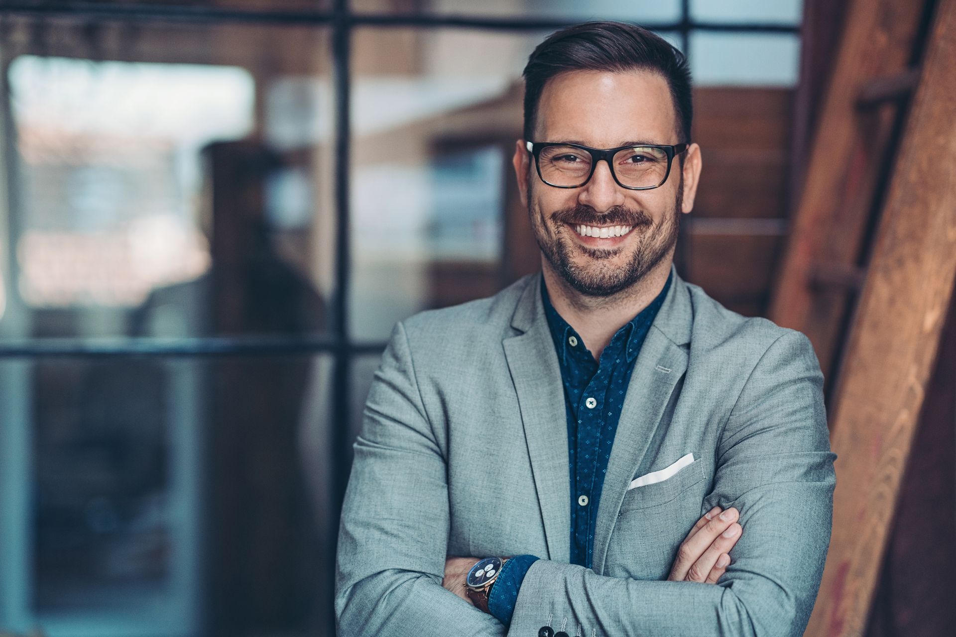 A man in a suit and glasses is smiling with his arms crossed.