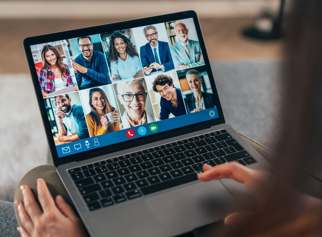 Person using a laptop for a video conference call with multiple people visible on the screen.
