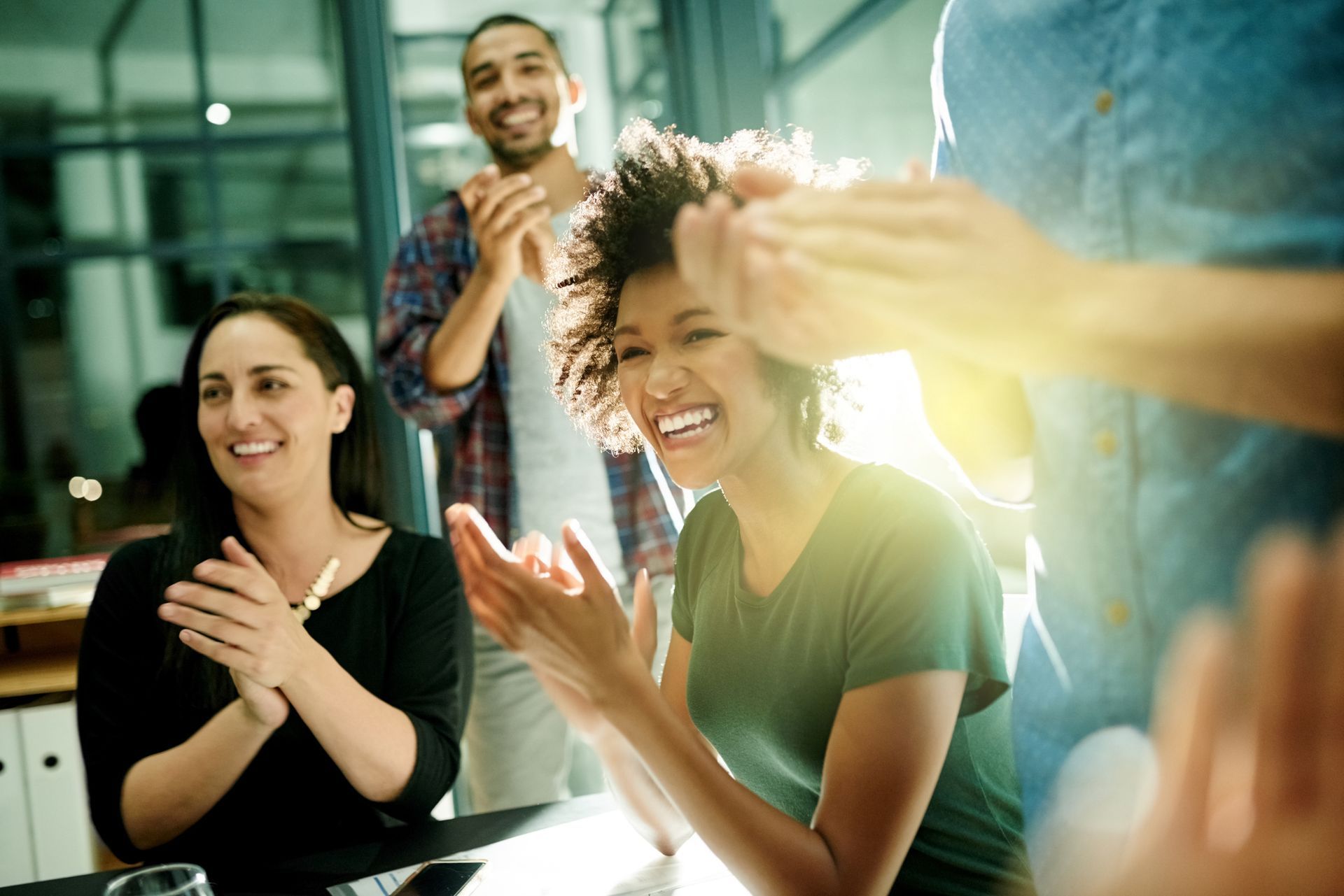 A group of people are sitting around a table clapping their hands.