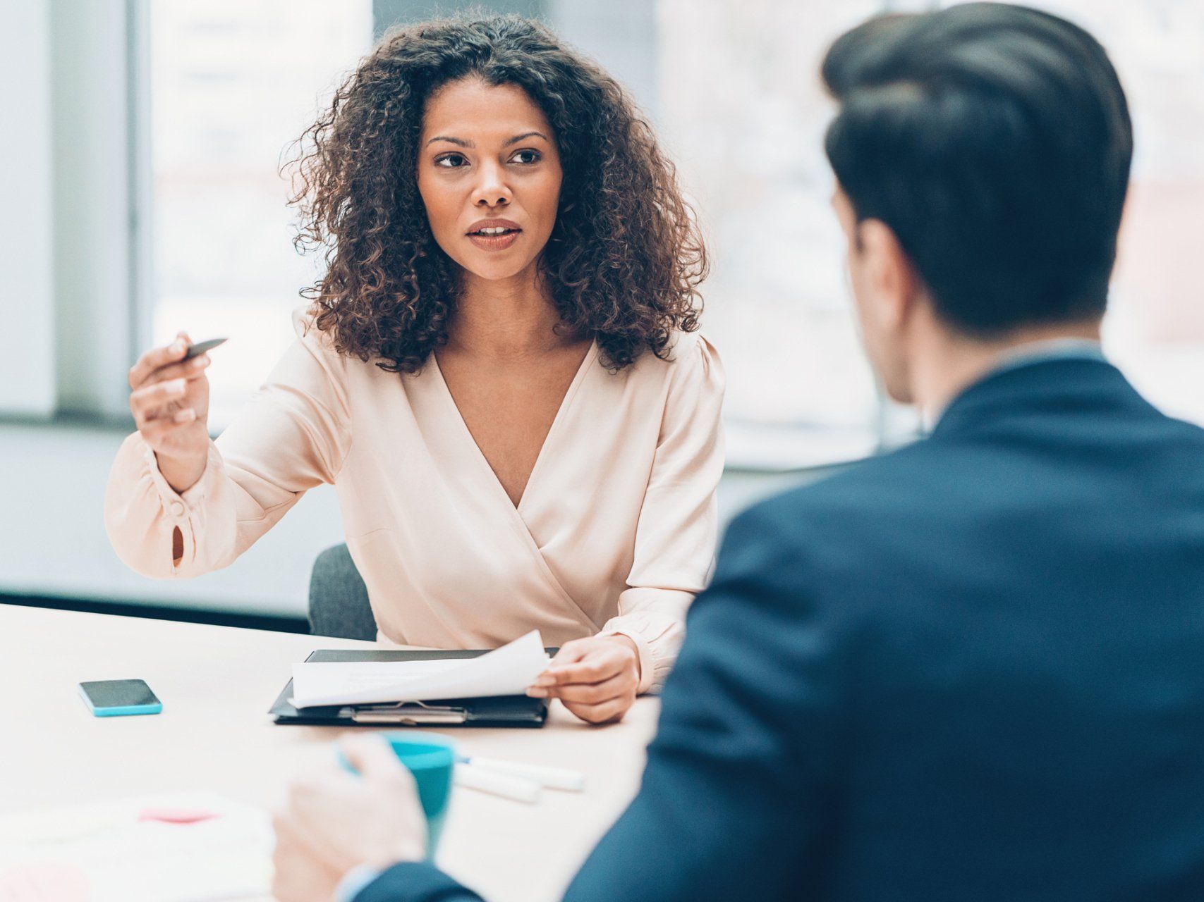 A woman with curly hair gestures while speaking to a man in a business setting.