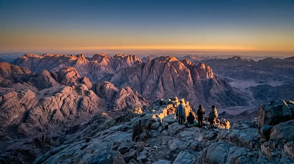 Sunrise from the summit of Mount Sinai in Egypt with travelers watching golden light strike the gran