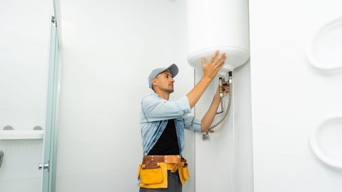 A man is fixing a water heater in a bathroom.
