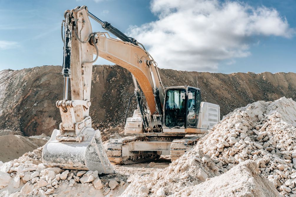 Yellow excavator in a quarry, scooping up white material.