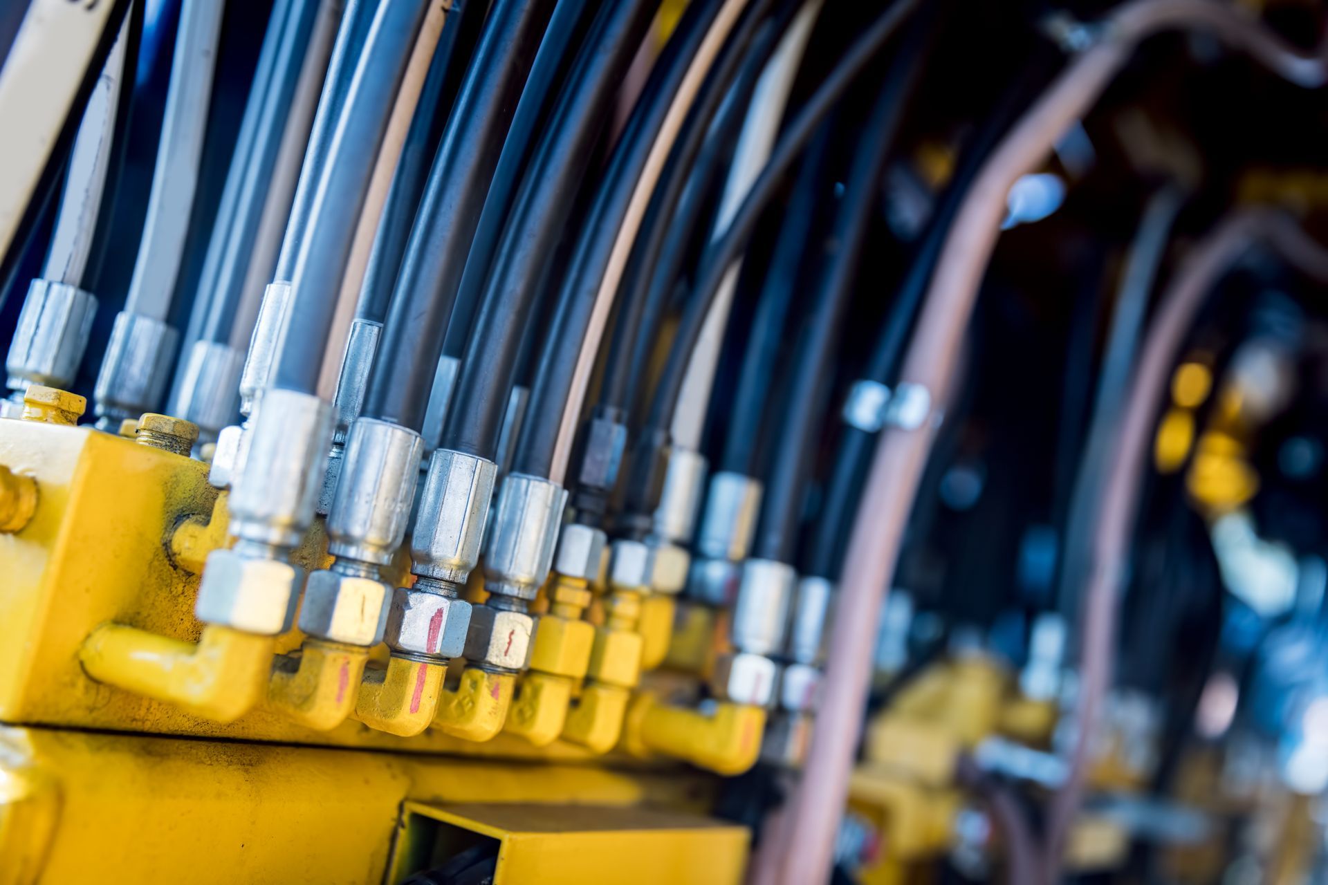 Close-up of yellow hydraulic equipment with black hoses and silver connectors.
