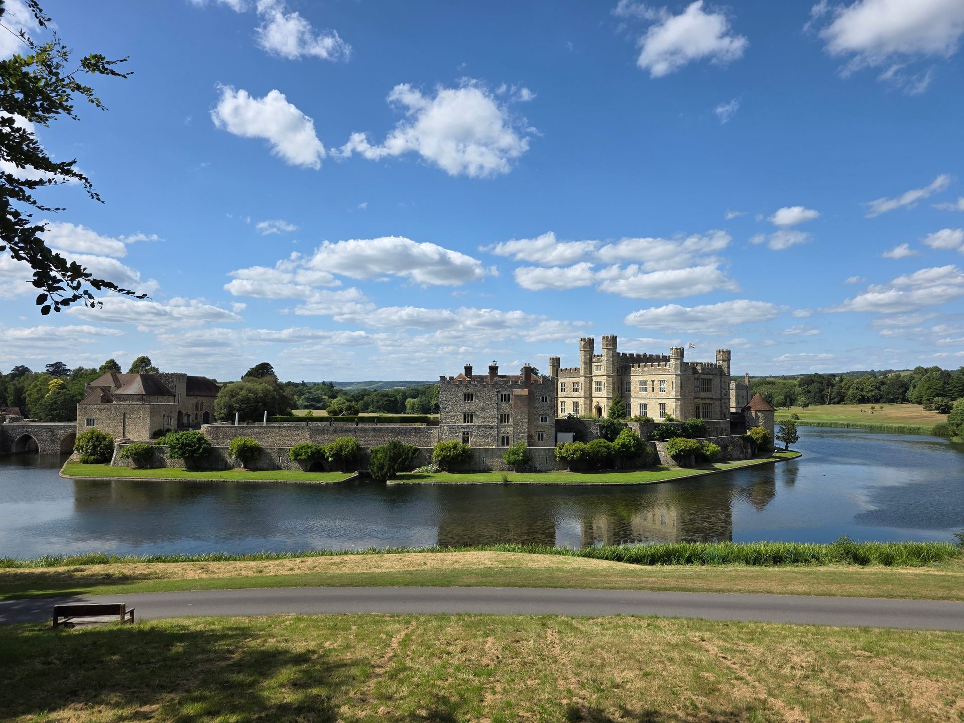 Leeds Castle, England, surrounded by moat on a sunny day with blue sky and clouds.